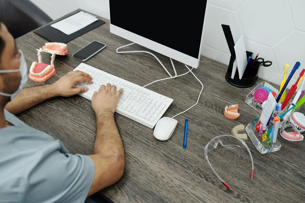 A dental team member typing at an office desk with dental models and a pen pot beside the keyboard